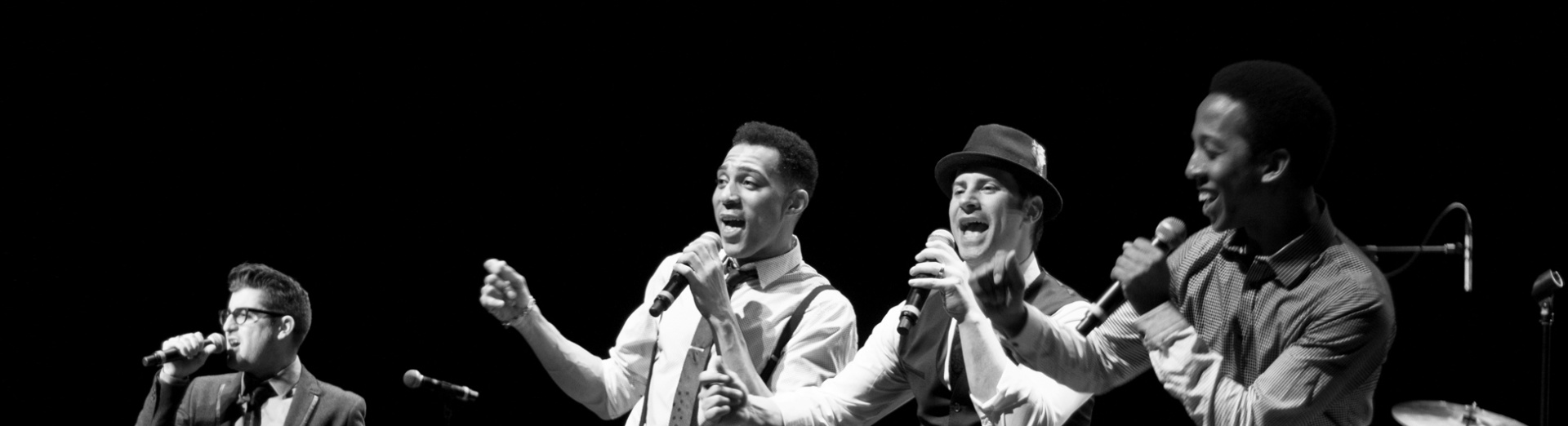 Members of The Doo Wop Project singing on stage against a dark background.