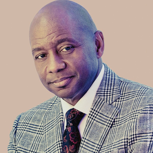 Branford Marsalis in a jacket and tie against a beige background.