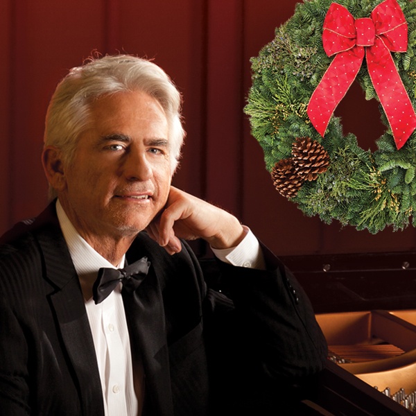 David Benoit in a black jacket and bow tie posing at the piano, a holiday wreath in the background.