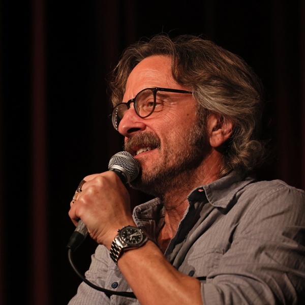 Marc Maron on stage, holding a microphone and looking at the audience.
