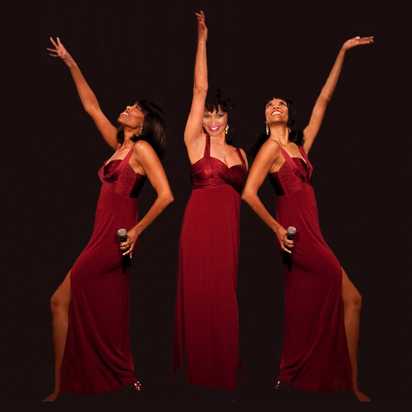 The three vocalist and performers of Supreme Reflections,in red gowns, holding microphones and striking a pose with their arms in the air.