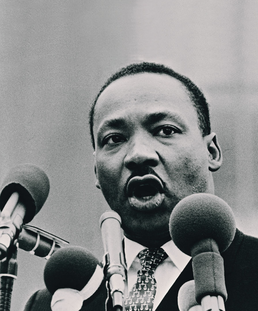 Black and white photograph of Dr. Martin Luther King, Jr. speaking into an array of microphones.