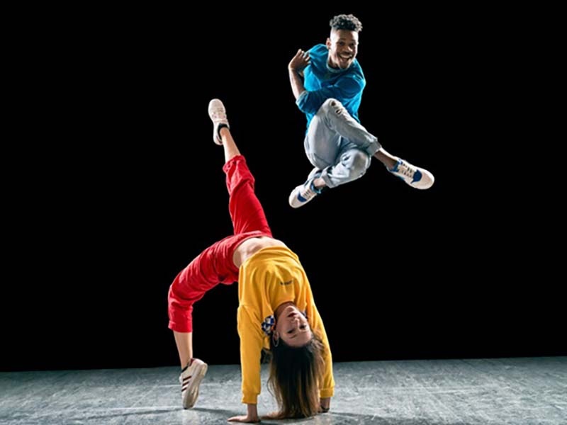 Two dancers from Versa-Style Dance Company on a stage, one jumping high in the air